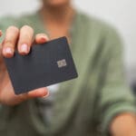 A close-up reveals a lady's hand displaying a dark credit card with a chip, ideal for contactless payments, illustrating online shopping and mobile banking.