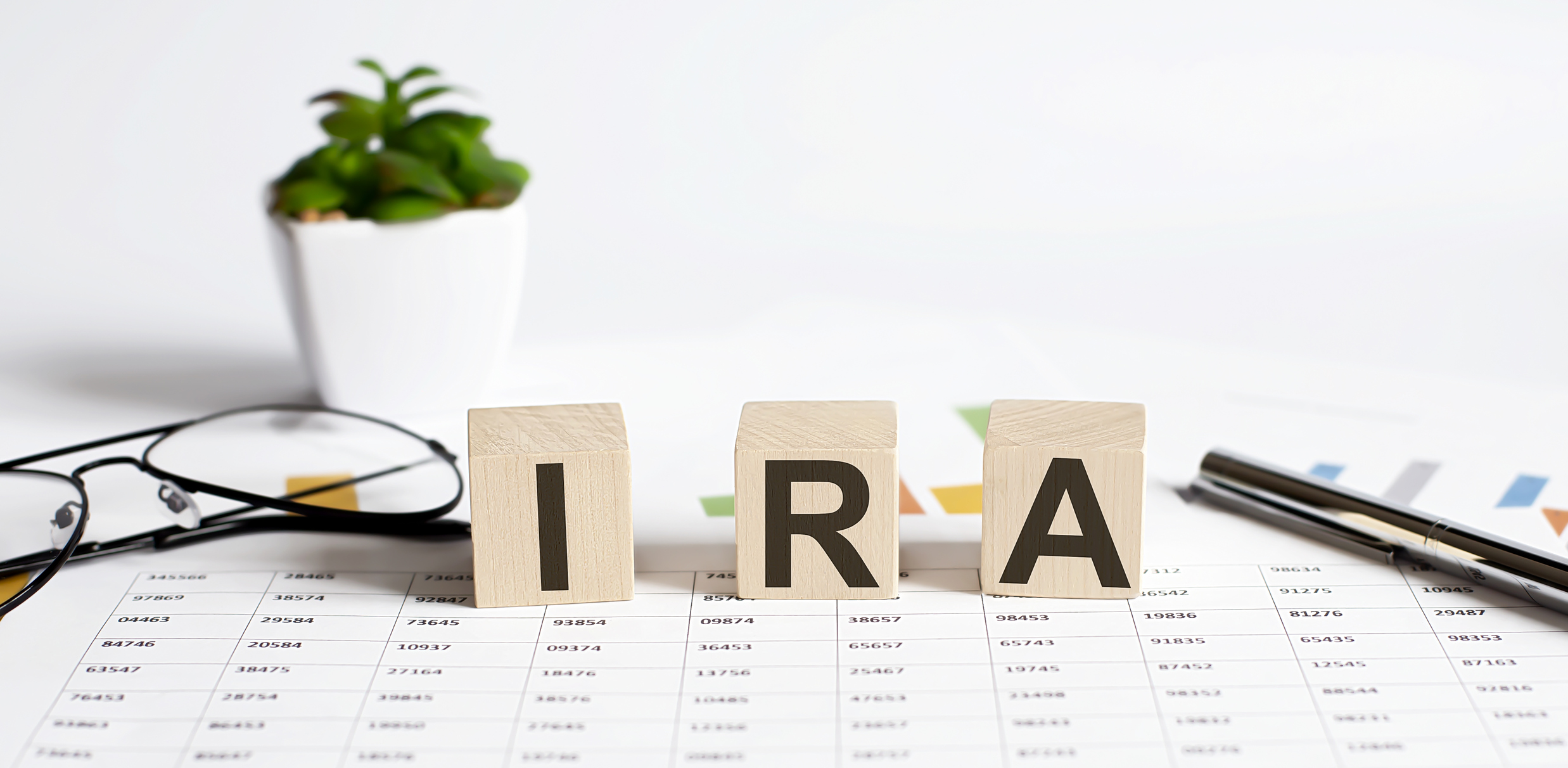 IRA word concept written on wooden blocks, cubes on a light table with flower ,pen and glasses on chart background