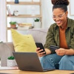 Happy black woman, credit card and online shopping on smartphone for digital payment, fintech account or finance at home. Female person, mobile banking and app for cash, ecommerce technology or money