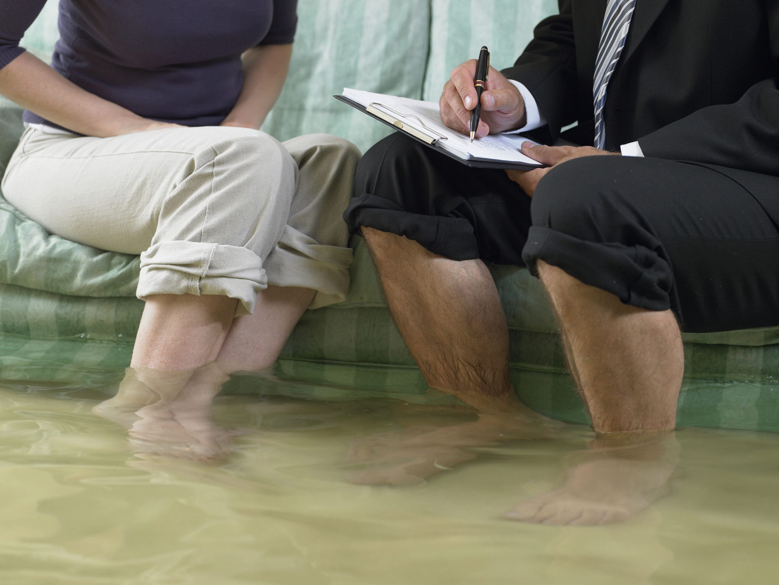 Mature man and mid adult woman sitting on sofa with water over their ankles, low section