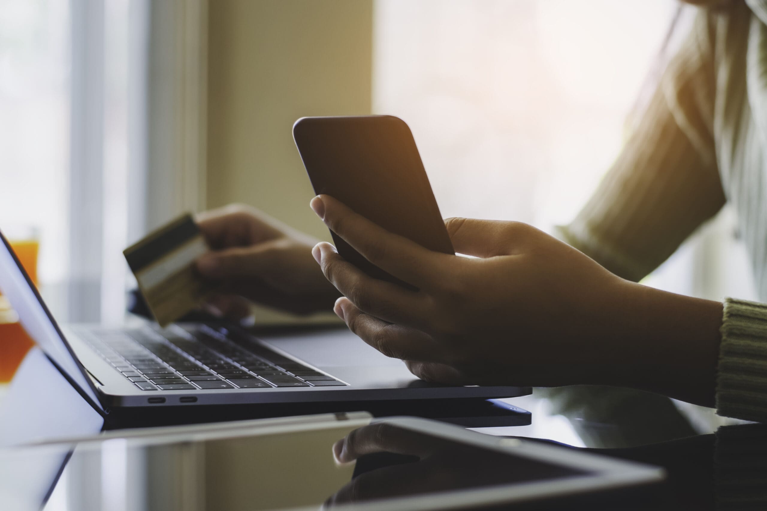 Woman make online shopping and payment by using mobile smart phone with credit card, work on laptop computer on the desk at home. Electronic digital marketing and technology concept.