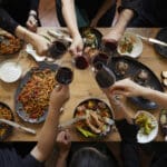 richly set dinner table from above with hands eating drinking and toasting