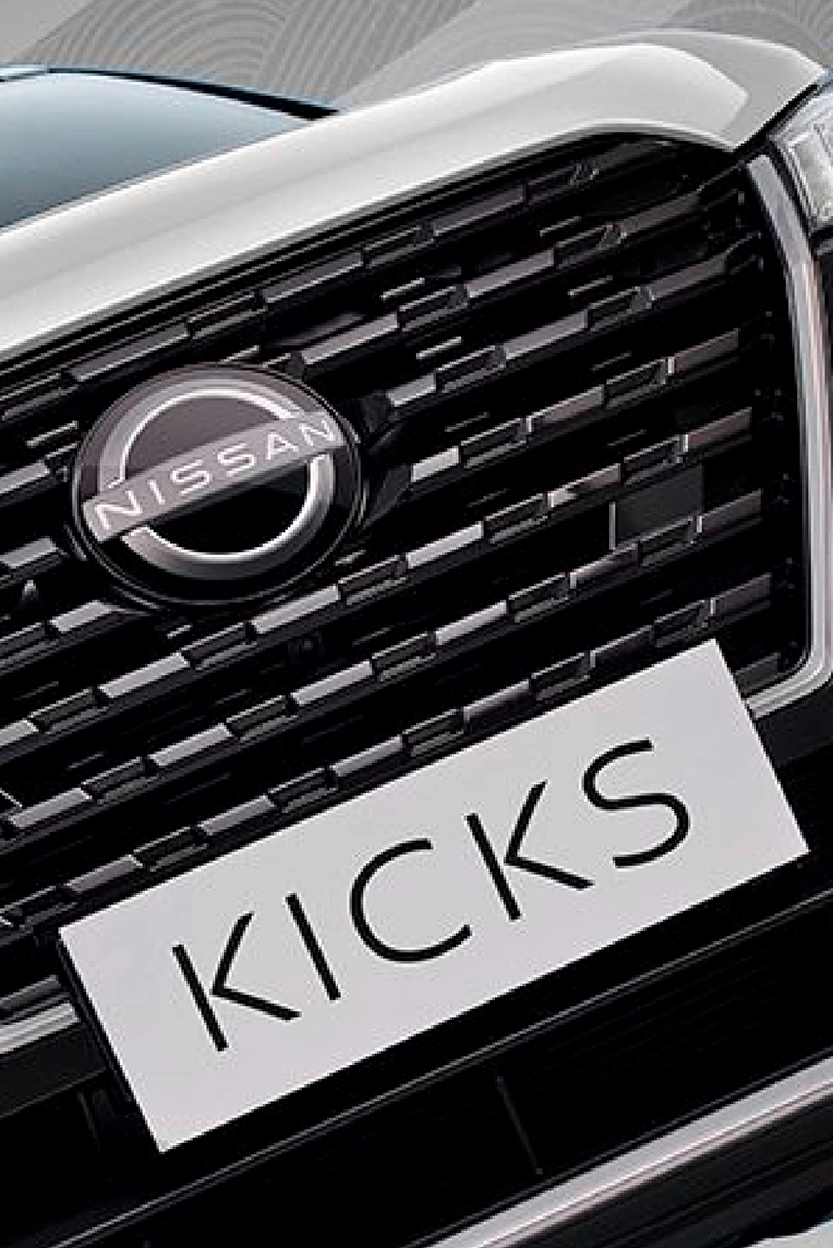 grade frontal de um Nissan Kicks branco e a placa do carro escrito kicks.