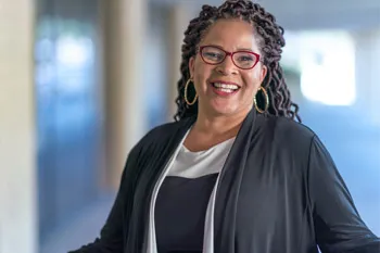 A woman with glasses and long dark braids smiles at the camera