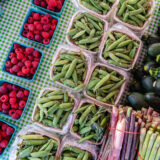 A top-down view of green peas and red raspberries in individual containers