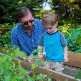 A child and his father spraying gardening beds with water