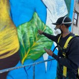 Man standing on elevated lift spray painting mural leaf.