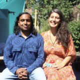 Two people with long dark hair pose for a photo outdoors on a sunny day