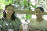 Two people in green and brown shirts, respectively, converse outdoors on a sunny day