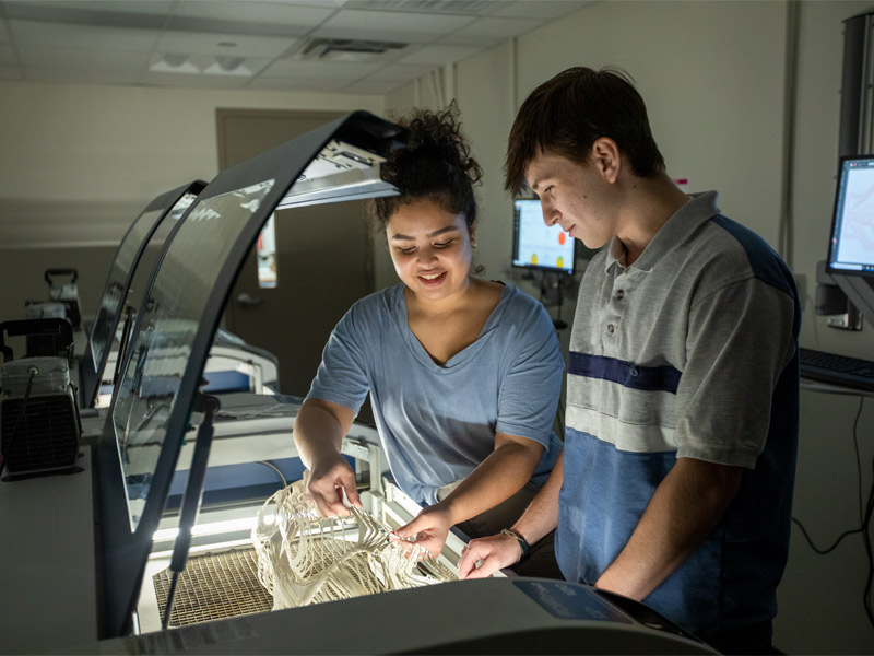 Two students working in a lab working with a fabrication machine. 