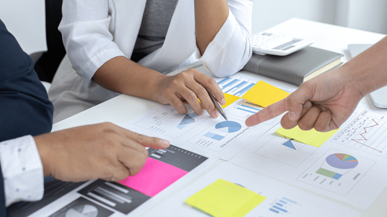 three people sitting around a table, pointing at charts