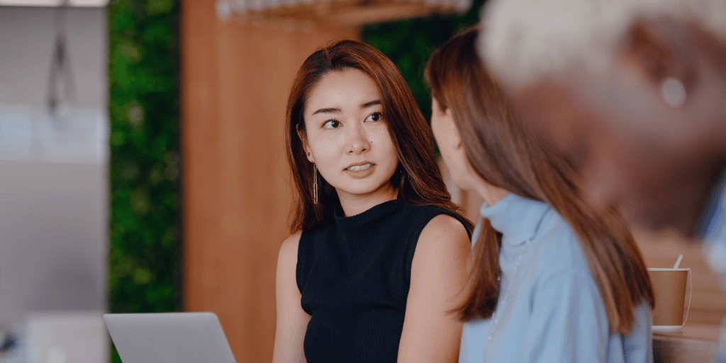 two women speaking together while sitting next to their laptops