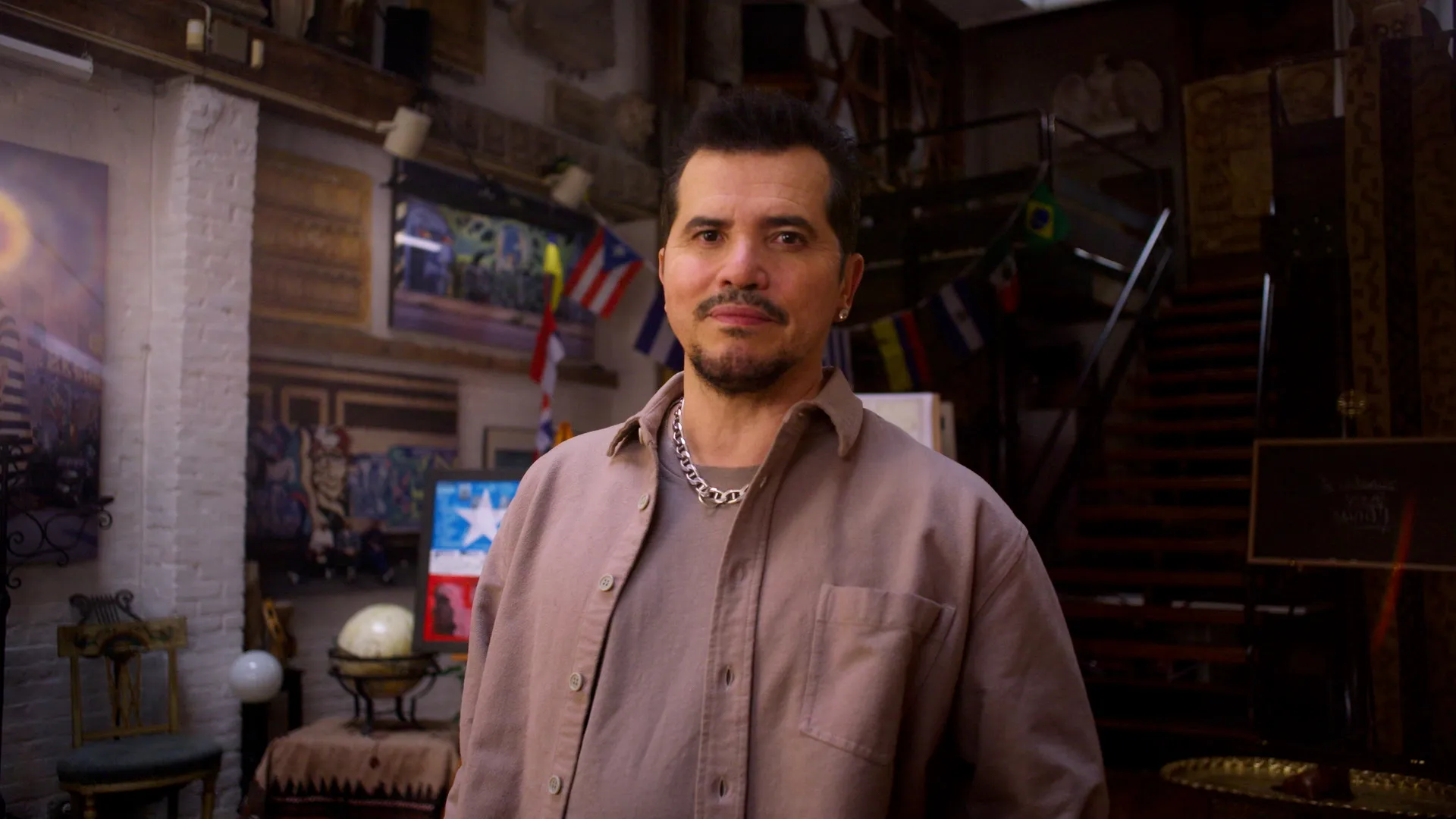 Man in beige jacket and black hair looks at camera