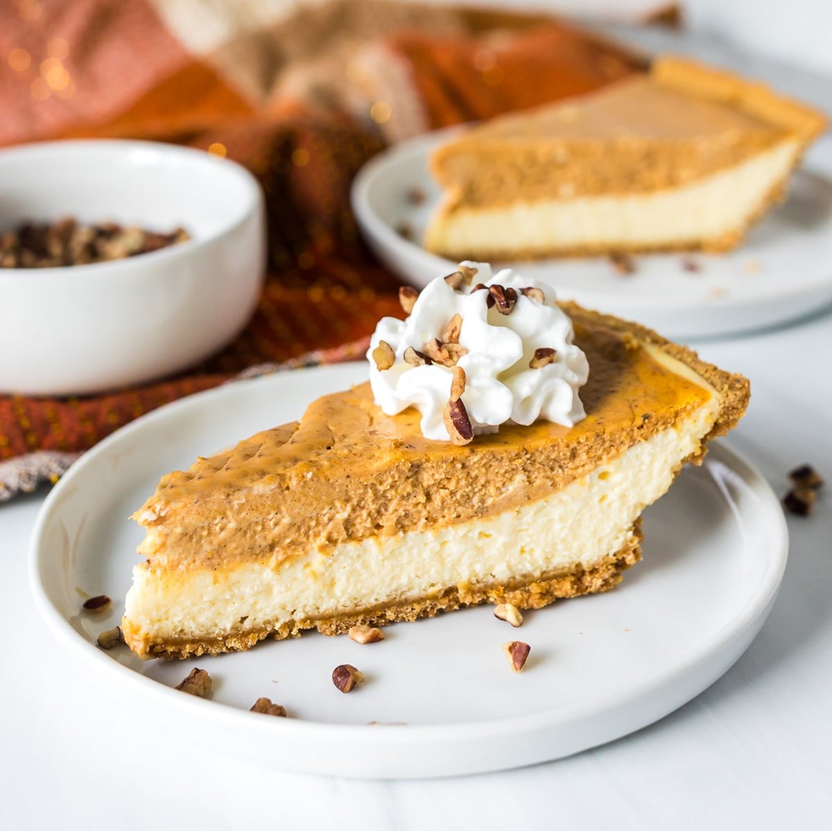 slice of layered pumpkin cheesecake topped with whipped cream on a white plate.