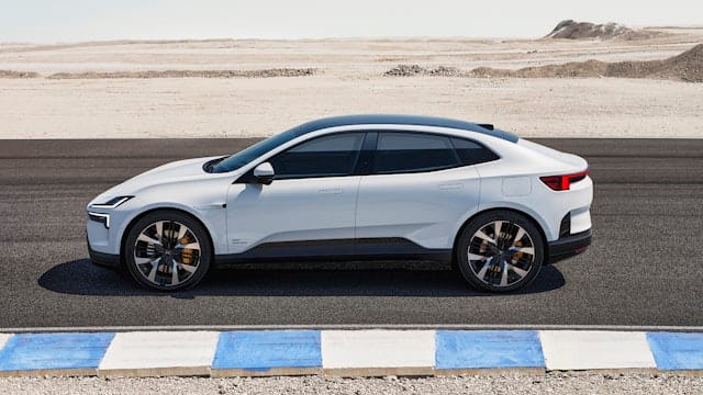 A white Polestar 4 electric SUV coupé is parked on a desert road next to a blue and white curb on a clear day.