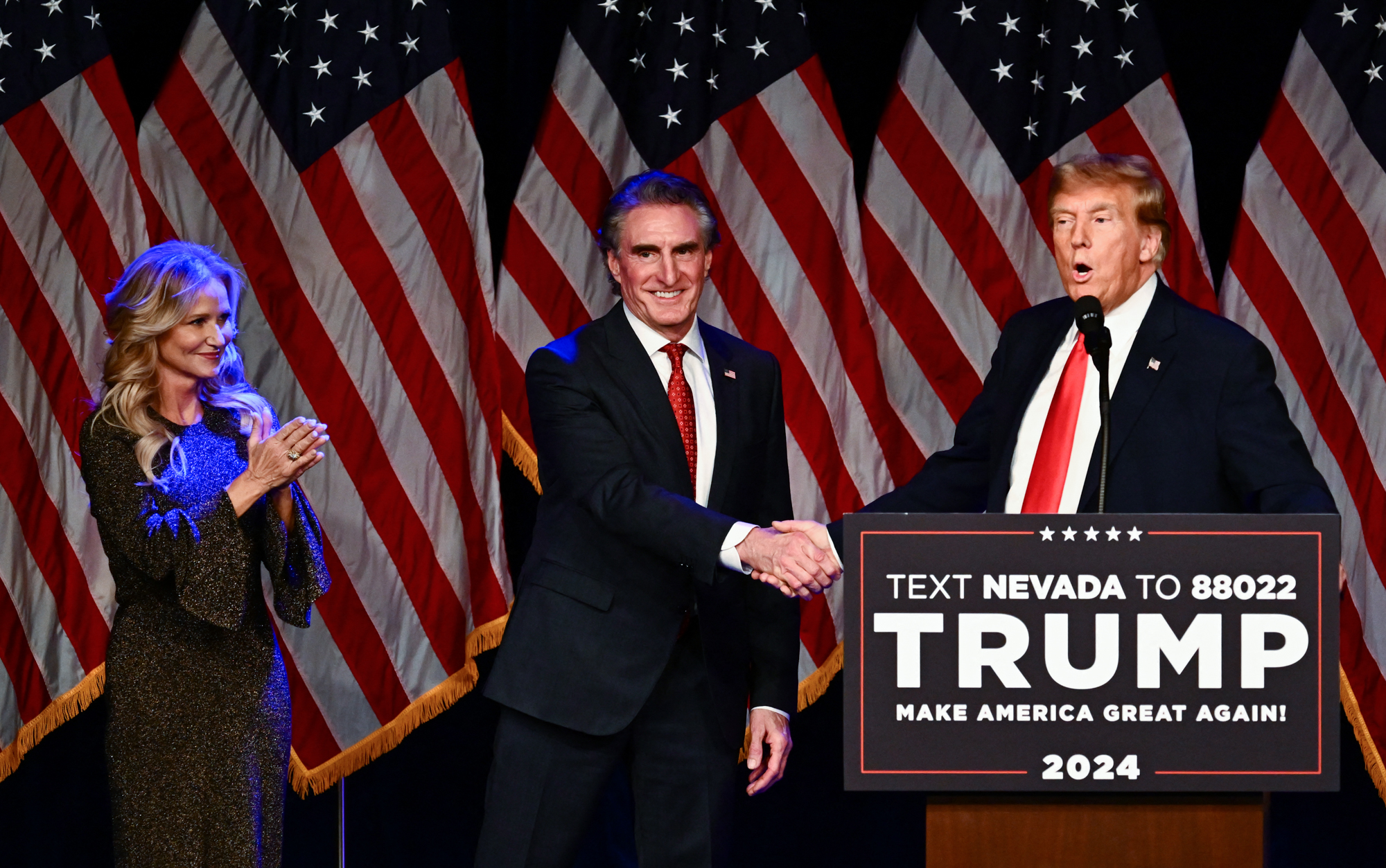 Doug Burgum shakes hands with Donald Trump, as his wife, Kathryn Burgum, applauds, during a Caucus Night watch party.
