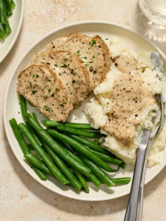 pork tenderloin with cream sauce on a white plate with mashed potatoes and green beans