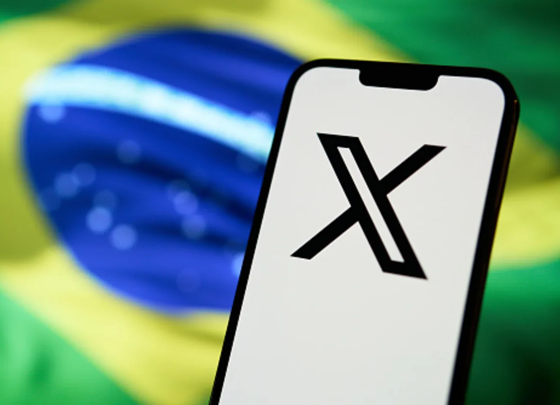 Smartphone displaying "X" logo in front of Brazilian flag.