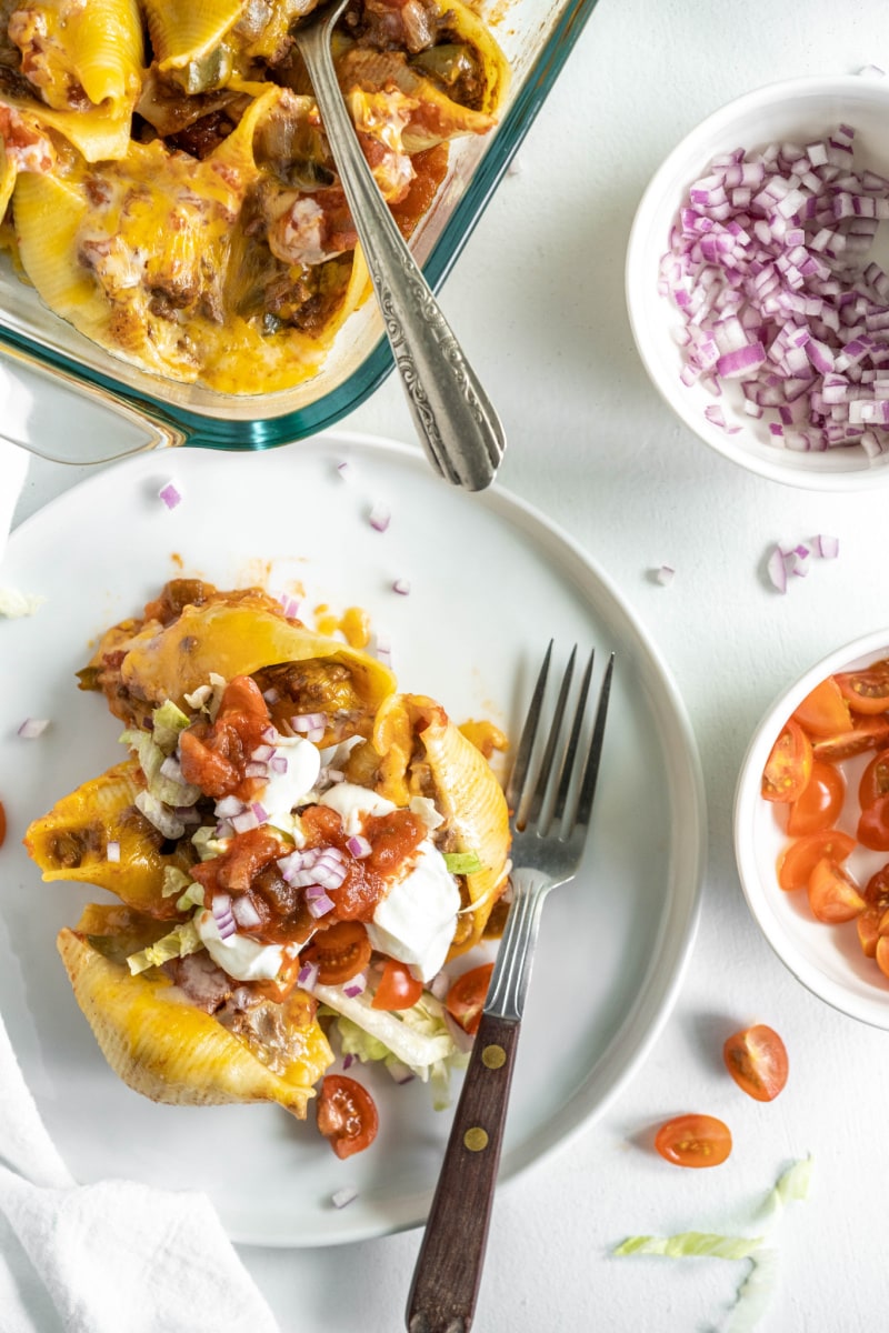 serving of taco stuffed shells on a plate topped with fixings