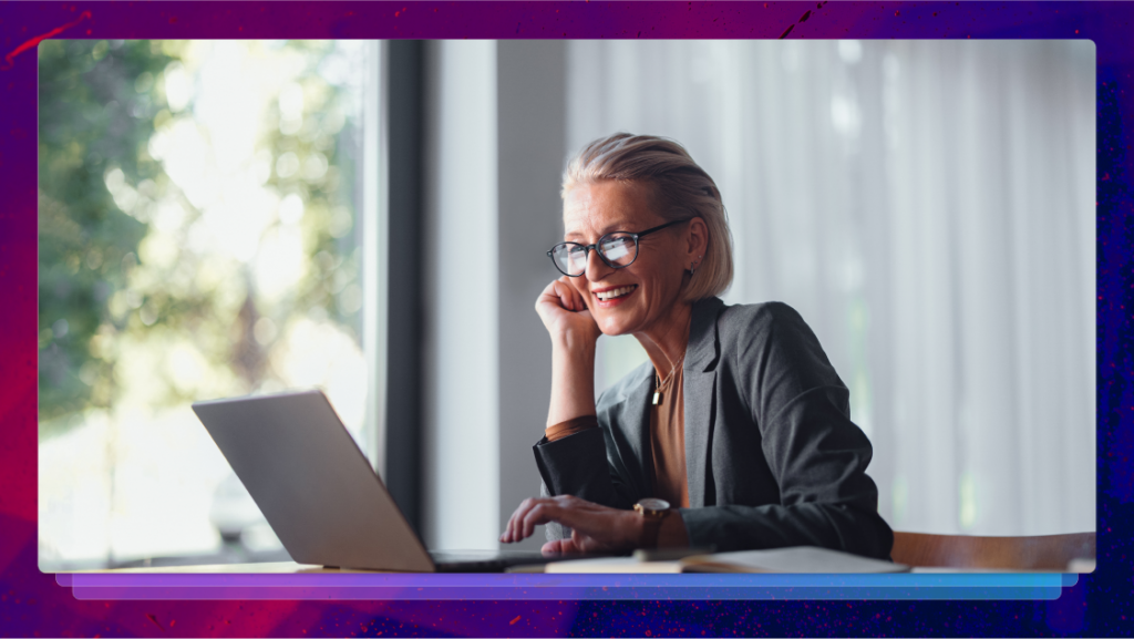 A smiling woman in business attire working on a laptop