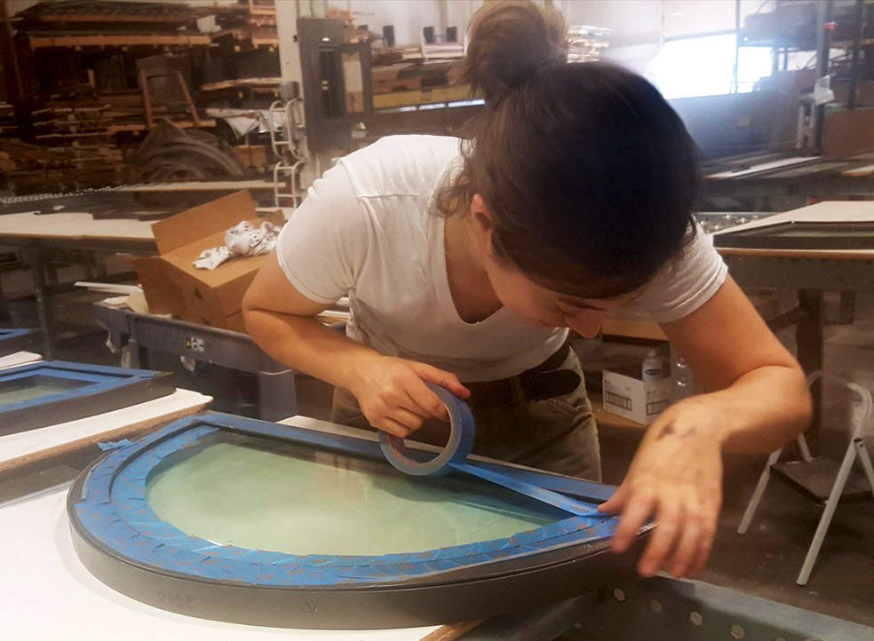 A woman masking the edges of a steel window frame with tape.