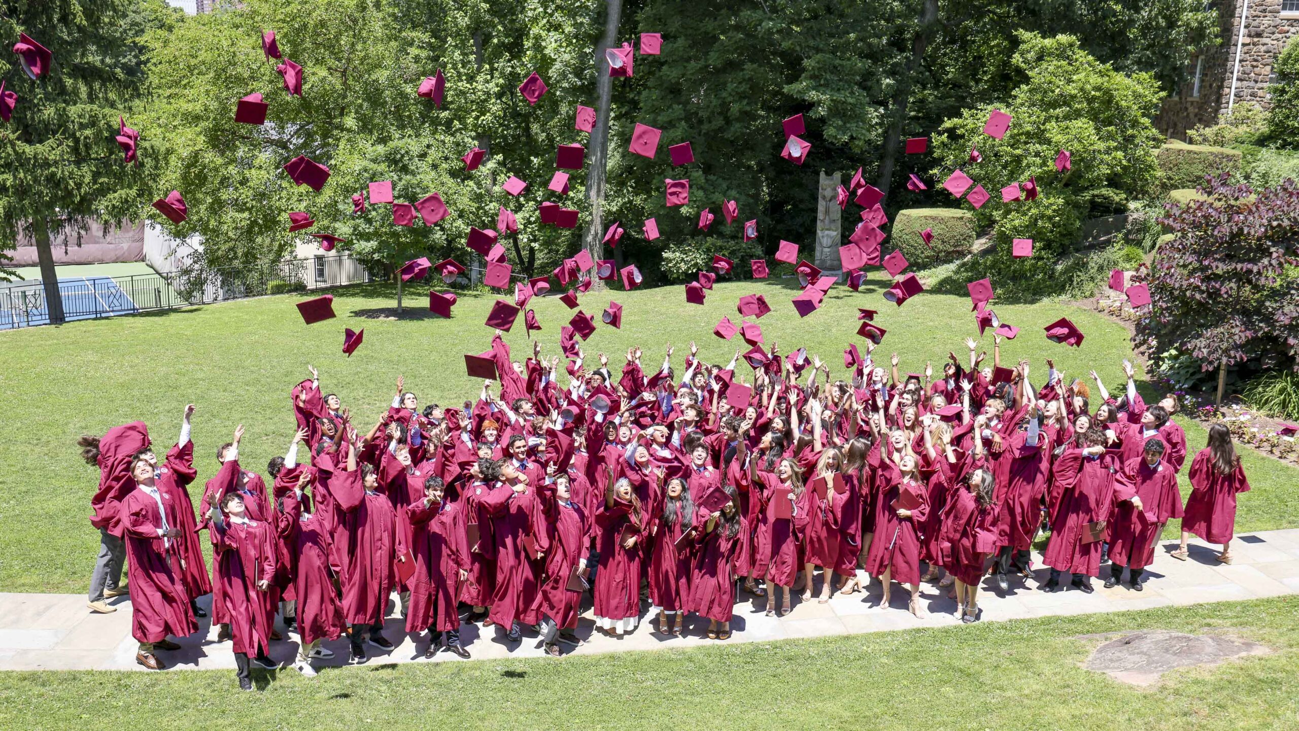 Students in graduation robes throw their caps in the air.