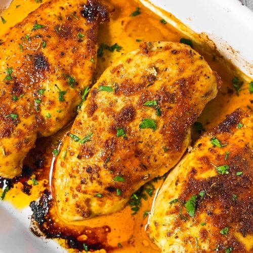 overhead view of three oven baked chicken breasts in white casserole dish