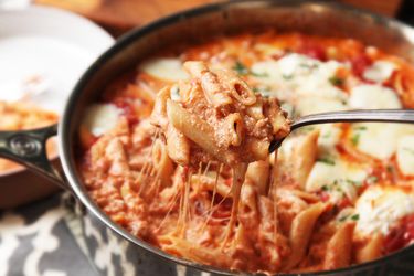 Creamy pasta being spooned out of a sauté pan.