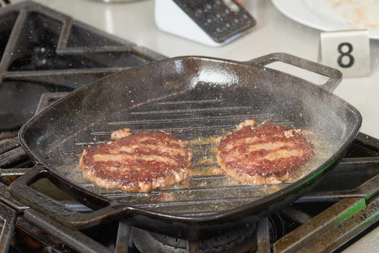 Two burger patties being cooked on the Victoria Cast Iron Square Grill Pan.