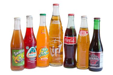 7 bottles of Mexican sodas, lined up on a white background