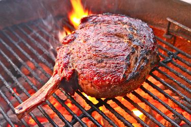 A large bone-in ribeye steak grilling on a charcoal grill.