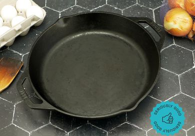 the lodge dual handled skillet on a black tile surface with a carton of eggs to the left and a bag of yellow onions on the right