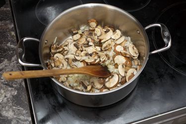 a rondeau on a stove with mushrooms and onions and a wooden spoon