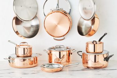 Several pieces of copper cookware on a marble kitchen countertop.