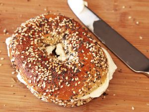 A bagel resting on a cutting board next to a knife with cream cheese spread in the center