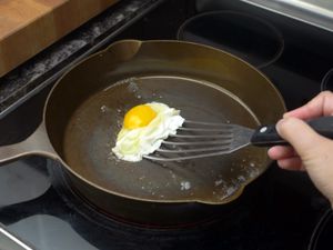 using a fish spatula to flip a fried egg in a cast iron skillet