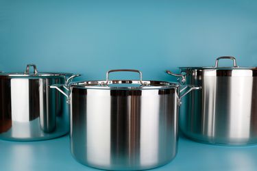 Three stainless steel stockpots on a blue surface