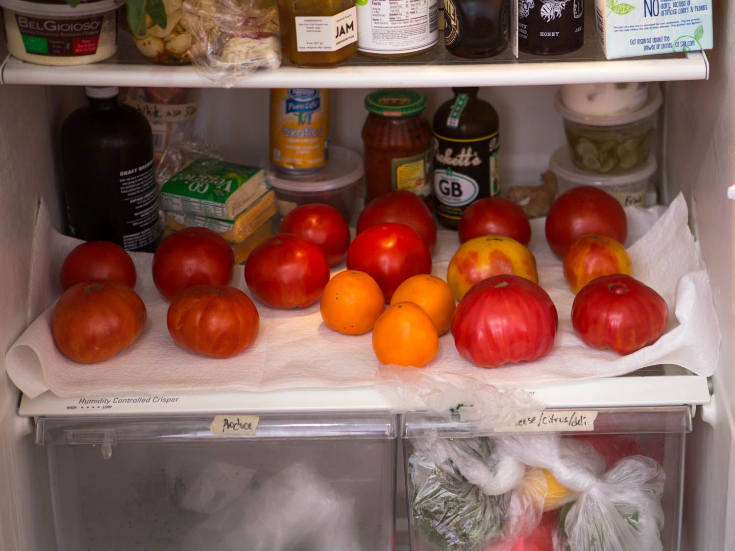 Tomatoes of various sizes, shapes, and colors lined up in a refrigerator. 