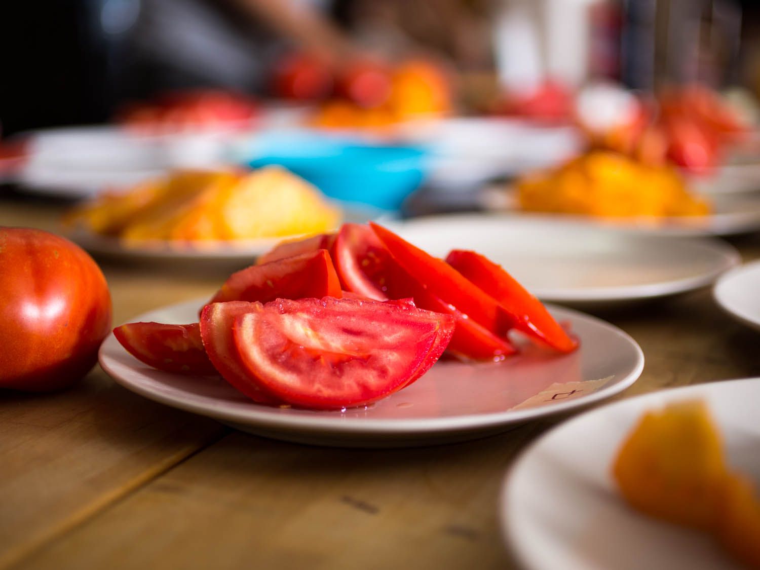 A tomato sliced and resting on a white plate with a whole tomato off to the side.