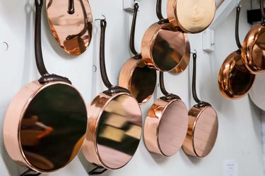 Copper pans hanging from hooks on white wall