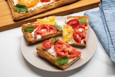 Slices of tomato tart on a plate, set in front of a cutting board with the rest of the tomato tart