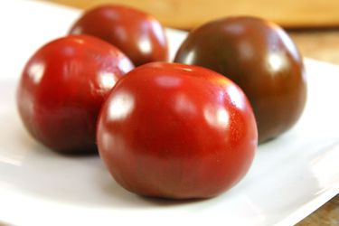 Whole ripe tomatoes on a plate with their top sides down.