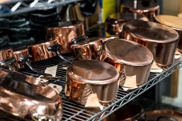 Copper cookware on a metal shelf.