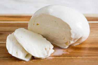 A ball of fresh mozzarella sliced open on a cutting board.