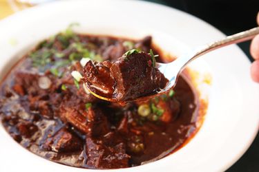 A spoonful of Texas chili con carne is held up to the camera. A bowl of chili is visible in the background.