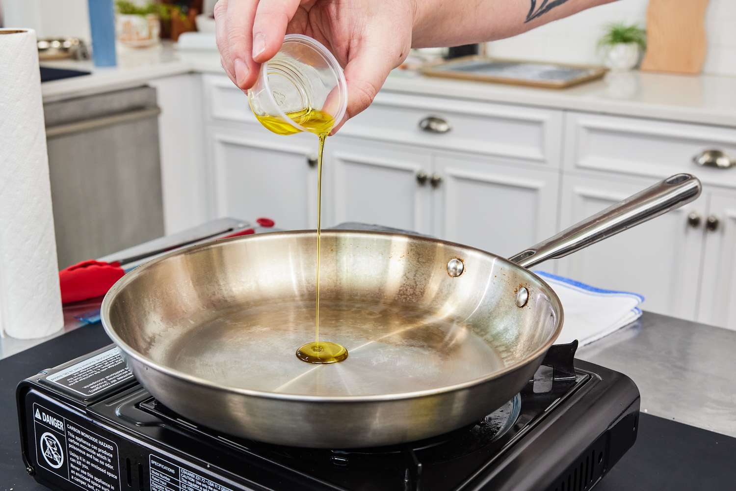 a hand pouring oil into a stainless steel skillet