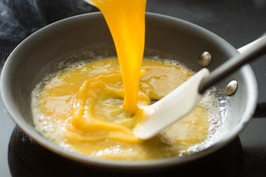 Pouring egg into a skillet for scrambled eggs and stirring with a flexible spatula