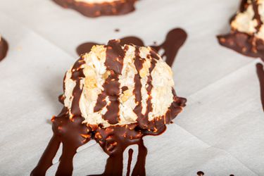 A chocolate-drizzled coconut macaroon on parchment paper.