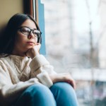 Sad teenage girl looking out the window on a cold autumn day