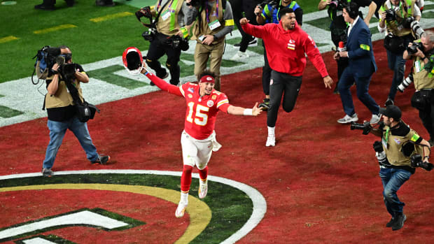 Patrick Mahomes runs with his arms out holding his helmet in the end zone as camera men run behind him